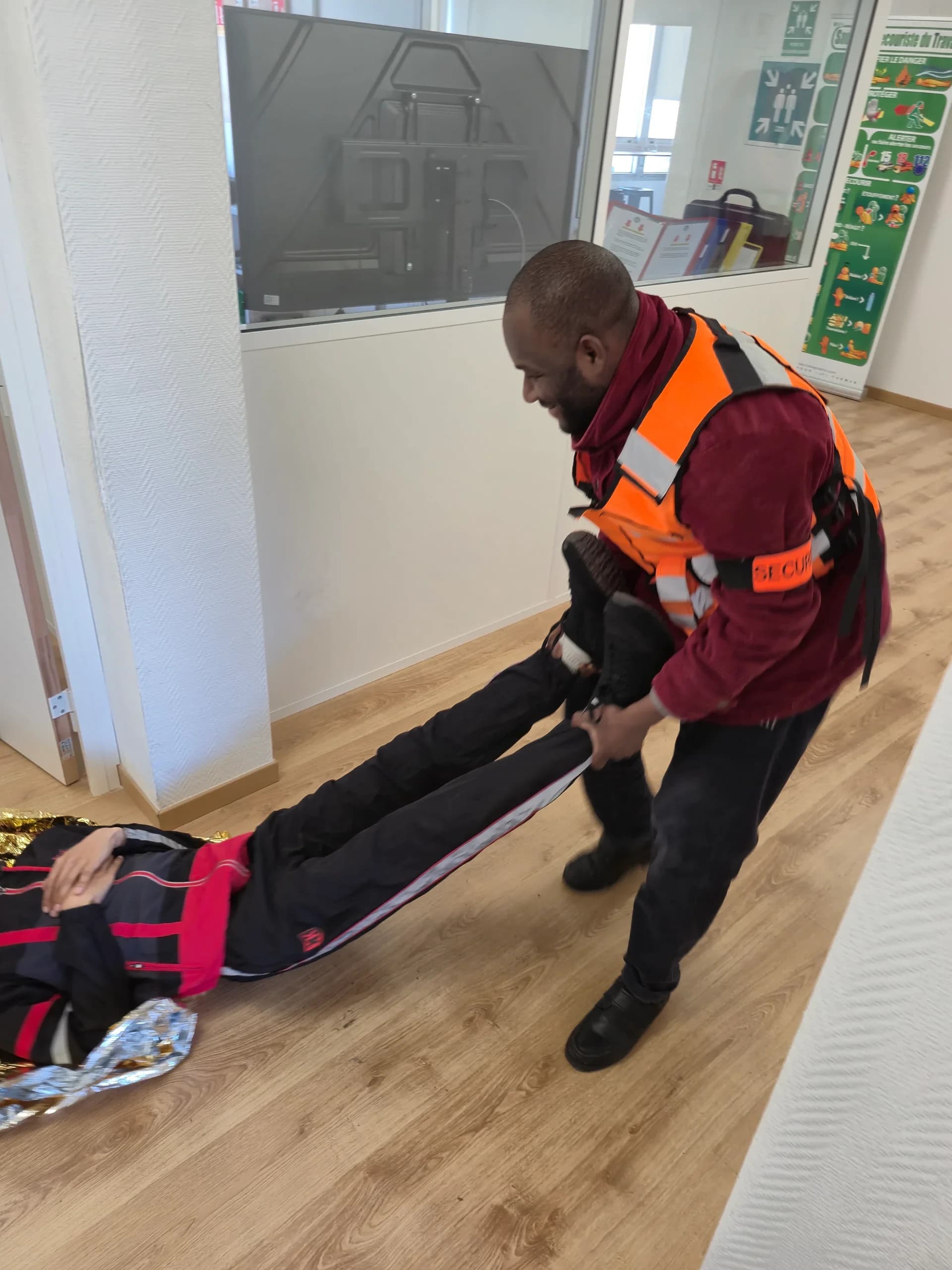 Stagiaire en gilet orange tirant une victime par les chevilles pour la dégager